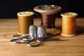 YELLOW OCHRE COTTON REELS WITH SCISSORS AND THIMBLES AND OLD VINTAGE WOODEN SPOOL AND THREAD IN BACKGROUND Royalty Free Stock Photo