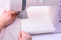 Female hands stitching light fabric on sewing machine at home.