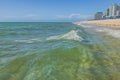 View of shoreline with architectural buildings under blue sky on horizon accompanied by gentle waves rolling onto sandy beach. Royalty Free Stock Photo