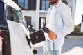 View from the side. Charging the vehicle. Young stylish man is with electric car at daytime Royalty Free Stock Photo