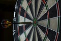Side view of professional darts board with arrow in bull`s eye in the dark Royalty Free Stock Photo