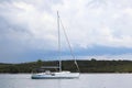 View from the side to the sailing yacht going under the motor past the green shore against the sky with storm clouds. Active rest