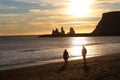 view of silhouetted people on a beach with shiny water  rocky cliffs against a sunny sunset sky Royalty Free Stock Photo