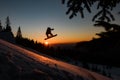 view of skier silhouette making jump in the air while sliding down snow-covered slope against the backdrop of sunset Royalty Free Stock Photo