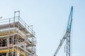 Scaffolding around the shell of a house with sky and crane in the background