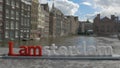 View of small plastic figure of Iamsterdam letters sculpture on the bridge against blurred cityscape, Amsterdam