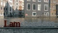 View of small plastic figure of Iamsterdam letters sculpture on the bridge against blurred cityscape, Amsterdam