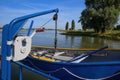 View on small rescue boat at crane of passenger ferry, trees, rural landscape and river Ijssel background against blue summer sky