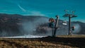 View of snow cannons or artificial snow makers on a ski slope on a sunny day. Visible partly covered ski slope with snow and some