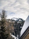 View of a snow covered mountain peak and pine forest during winter, chalet roof in foreground Royalty Free Stock Photo