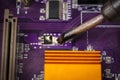 View of the soldering iron tip and the purple computer motherboard