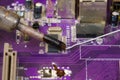 A view of the soldering iron tip, tin, and the purple computer motherboard