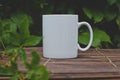 A solo blank white coffee mug on the wooden table in the garden