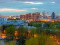 View of the spring evening city with blossoming trees, the setting sun and lights