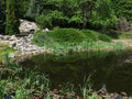 View of spring vegetation around decorative garden pond with dried artificial waterfall made of rocks Royalty Free Stock Photo