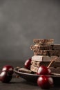 View of stack of chocolate bars in plate on wooden table with cherries, selective focus, gray background, Royalty Free Stock Photo