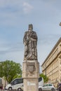 View of the statue of D. Dinis, in the square of the University of Coimbra, surrounding buildings, people and vehicles, cloudy sky