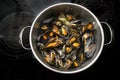 View into a steel pot with freshly cooked mussels, onions and herbs on a black stove for a Mediterranean seafood meal, copy space