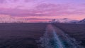 View from the stern of cruise ship with the vessel\'s wake in arctic sea, snow-covered mountains and purple colored sky. Royalty Free Stock Photo