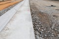 View straight down a section of extruded concrete curb, street construction detail with gravel and dirt