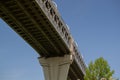 View of the structure of the highway bridge from below against the blue sky. The road passes over the city, over the green trees