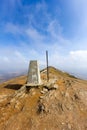 A view of the summit trig point of a Scottish mountain Ben Vorlich with eroded rocky soil under a majestic blue sky and altitude