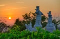 View of the sunset from a Buddhist temple on the mountain. Golden sky. Marble statues of warriors in the middle of the trees