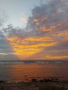 A view of the sunset sky over the open sea emitting golden rays of triangular shape seen from a beach.