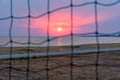 View of the sunset through the volleyball net. Dramatic sunset over sea.