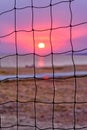 View of the sunset through the volleyball net. Dramatic sunset over sea.