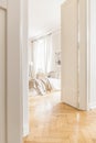 View through tall, open white door on a stylish, bright bedroom