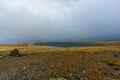 A view of a tarn mountian lake on a stony and grassy mountain plateau with a small cairn under a dark stormy sky