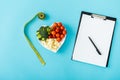 View of tasty vegetables on heart-shape plate near measuring tape, stethoscope and blank clipboard on blue Royalty Free Stock Photo