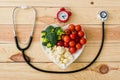 View of tasty vegetables on heart-shape plate near stethoscope and retro alarm clock on wooden surface Royalty Free Stock Photo