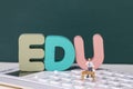 View of teacher figurine standing on a calculator around EDU letters