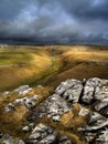 View of thick clouds over grassy and rocky hills and agricultural fields in countryside in autumn