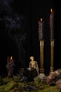 View of three burning black candles on table with concoction and smoke, skeleton on moss and spiders