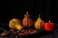 View of three pumpkins with orange candle on tablecloth and black background, horizontal