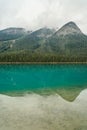 Perfect reflection of three mountain peaks, partially obscured by clouds in the rippling water of Emerald Lake - vertical