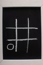 View of tic tac toe game on blackboard with chalk grid and naught on wooden surface