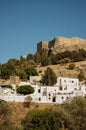 A view to a little village Lindos on a hill which is full of white houses located in Rhodes, Greece. An old castle on the backgrou Royalty Free Stock Photo
