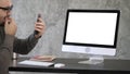 Attractive beard man checks his teeth on his phones selfie camera near computer monitor. White Display. Royalty Free Stock Photo