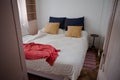 View to small cozy bedroom in old apartment through the open door. Bed covered with white blanket, blue and beige pillows