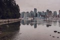 View to Stanley park seawall, skyscrapers and harbour reflexting in the water on overcast winter day. Vancouver, British Columbia