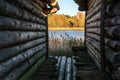 View to the tranquil blue lake, orange autumn trees and reeds through the narrow lane between two old log huts