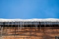 View to the wooden wall and snow roof of house with icicles and blue sky