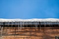 View to the wooden wall and snow roof of house with icicles and blue sky.