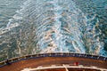 View from the top at the back deck of the cruise ship, leaving foamy trace on the water and waves in the ocean during sunset.