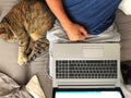 View from top of a man working from home due to covid 19 with a laptop and a cat sleeping on his side Royalty Free Stock Photo