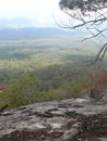 A view from the top of a mountain with a large bolder and dry trees and ashes from a recent fire